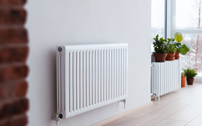 White radiator installed on a wall with potted plants nearby.